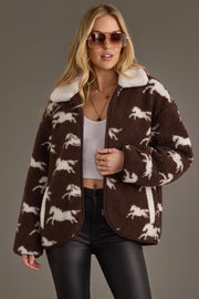 A woman wearing sunglasses, a white crop top, black pants, and the Panache Apparel Collection Brown & White Fleece Horse Jacket stands against a plain background.