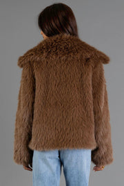 A person faces away from the camera wearing the Panache Apparel Collection Light Brown Faux Fur Jacket paired with light blue jeans, standing against a plain gray background.