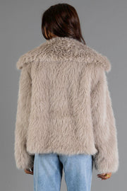 A person faces away from the camera, wearing the Panache Apparel Collection Taupe Faux Fur Jacket with light blue jeans against a plain gray background.