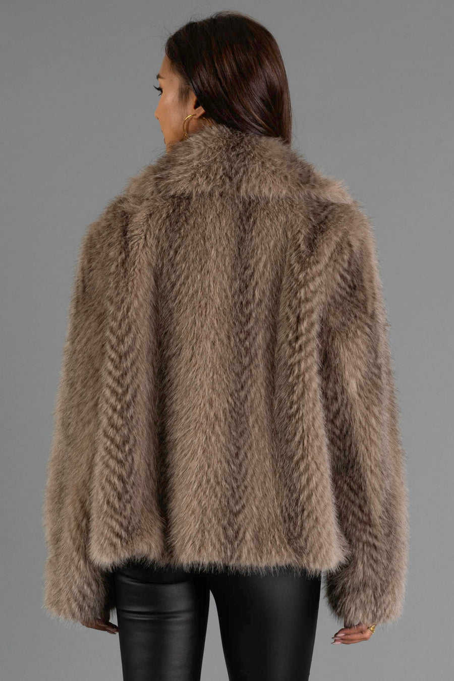A person with long dark hair is shown from the back, wearing the Panache Apparel Collection Two Tone Faux Fur Jacket and black leather pants against a plain gray background.