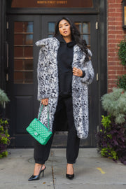 A woman wearing a Leopard Faux Fur Maxi Coat over a black hoodie and joggers, carrying a green quilted handbag and wearing black high-heeled pumps.