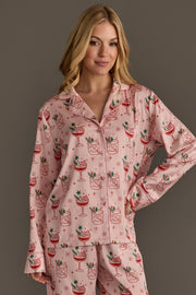 A woman wearing a Light Pink Christmas Cocktails Satin Pajama Set in light pink satin with a repeating pattern of holiday cocktails, lime slices, and stars.