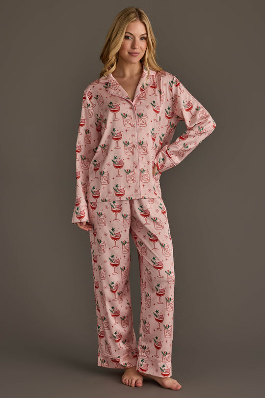 A person wearing a Light Pink Christmas Cocktails Satin Pajama Set in light pink, featuring a repeating print of cocktail glasses decorated with festive elements.