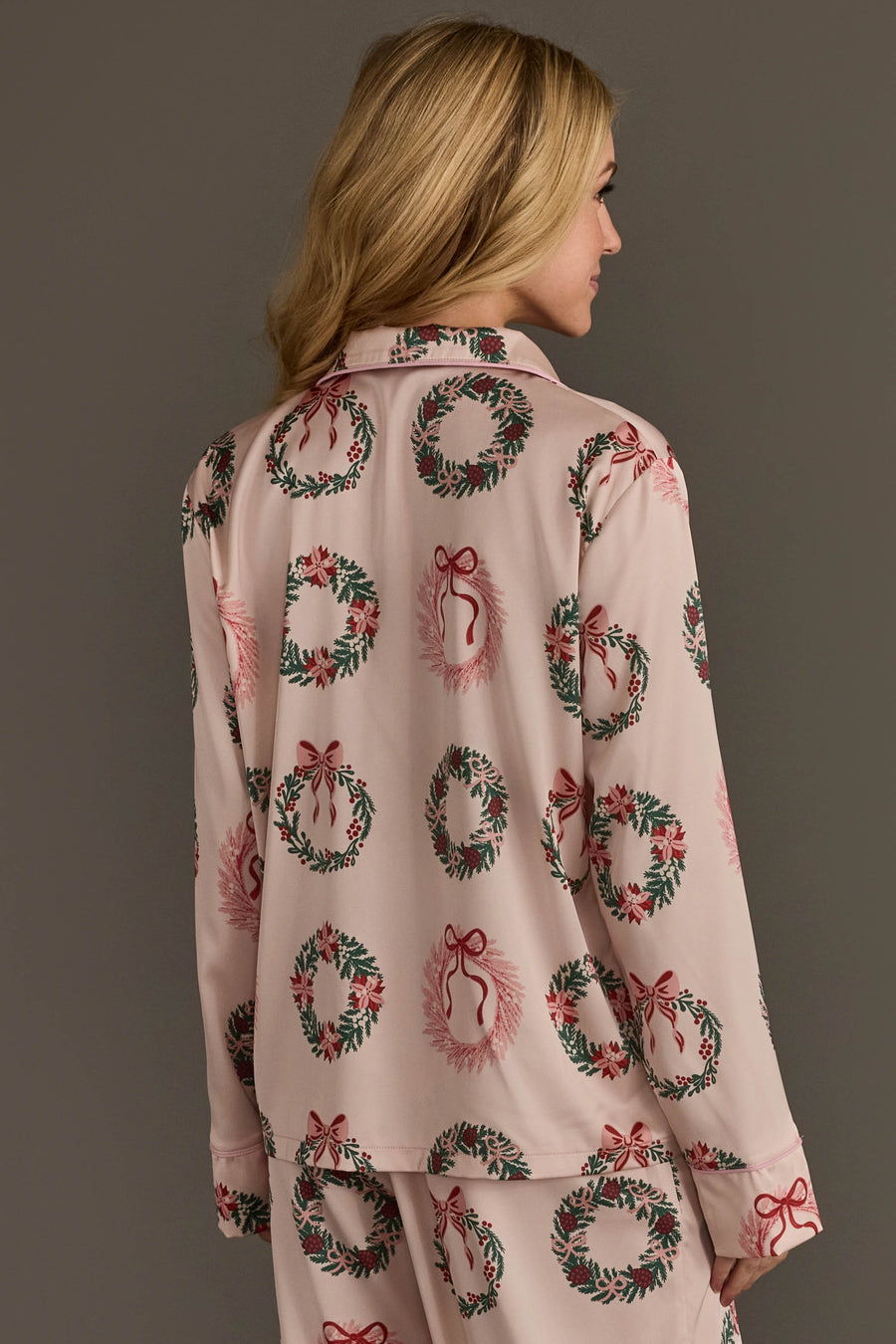 A person seen from behind wearing the light pink Christmas Wreaths Satin Pajama Set by Panache Apparel Collection, featuring a long-sleeved top patterned with wreaths and bows.