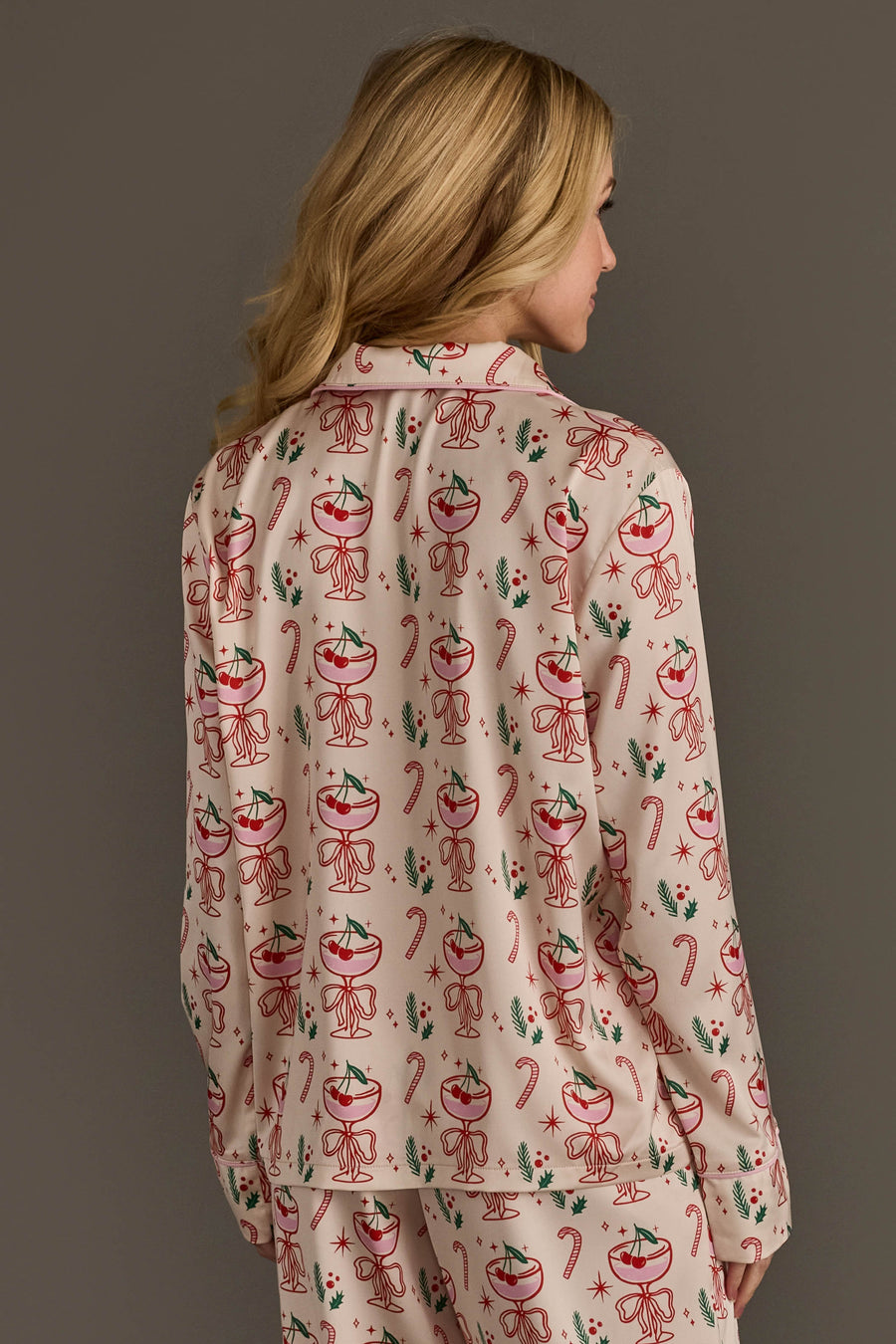 A woman wearing the Ivory Christmas Cocktails Satin Pajama Set, featuring ivory long-sleeved pajamas with a festive print of cocktail glasses, candy canes, and holly.