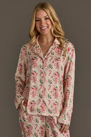 A woman wearing an Ivory Christmas Cocktails Satin Pajama Set, consisting of ivory long-sleeved pajamas with a festive cocktail print of glasses, cherries, candy canes, and holly leaves.