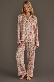 A woman wears an ivory Christmas Cocktails Satin Pajama Set featuring a festive print of candy canes, cocktail glasses, and greenery for holiday lounging.