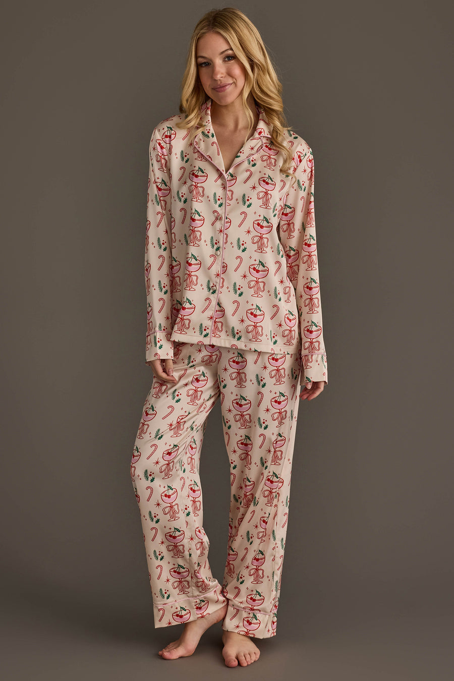 A woman wears an ivory Christmas Cocktails Satin Pajama Set featuring a festive print of candy canes, cocktail glasses, and greenery for holiday lounging.