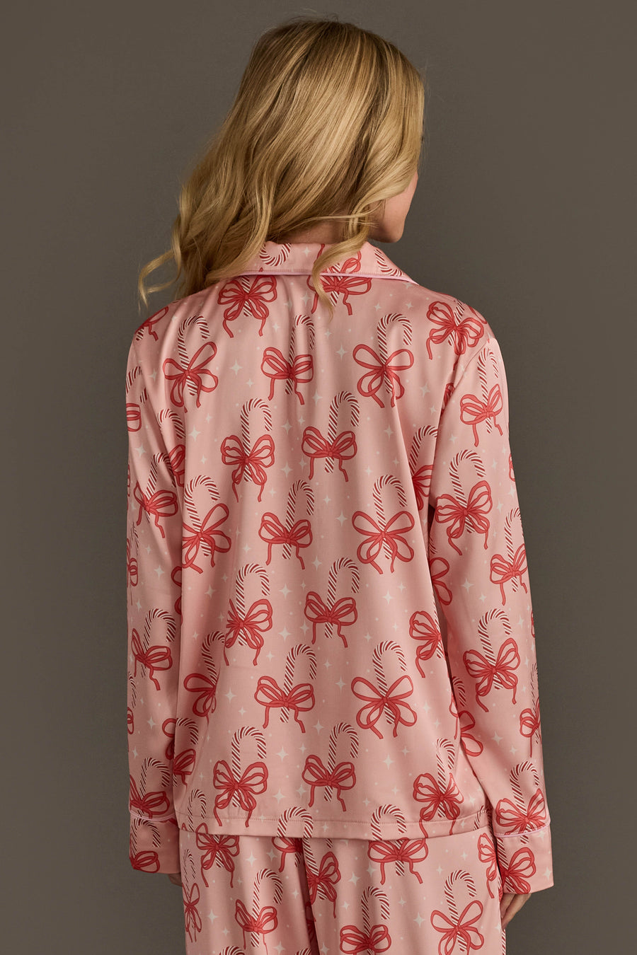A person seen from behind wearing the light pink satin Candy Canes & Bows Satin Pajama Set featuring a holiday candy cane print.