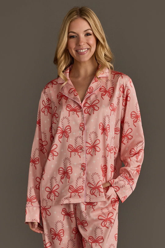 A smiling woman wearing a pink Candy Canes & Bows Satin Pajama Set patterned with red bows and candy canes.