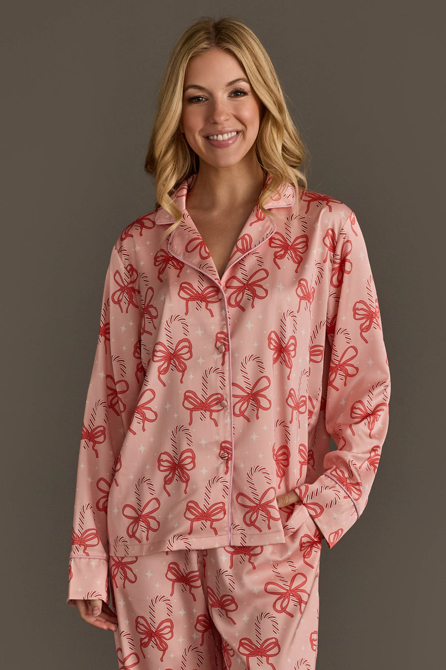 A smiling woman wearing a pink Candy Canes & Bows Satin Pajama Set patterned with red bows and candy canes.