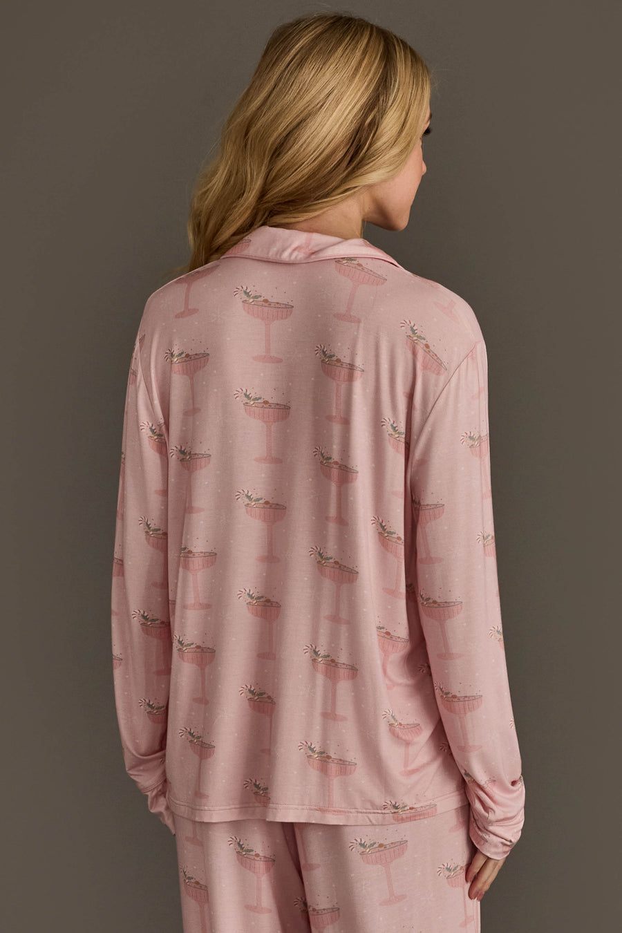 A person seen from behind wearing a light pink Christmas Cocktails Jersey Pajama Set featuring a repeating cocktail glass pattern.