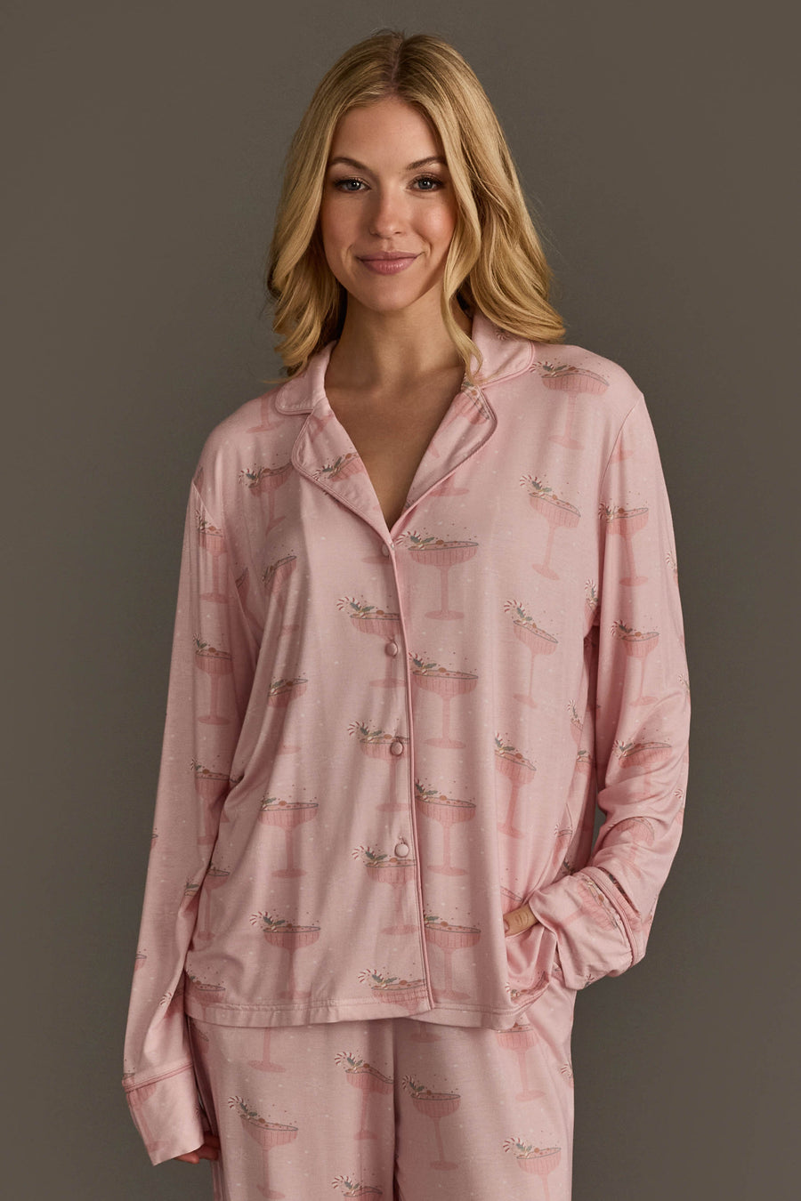 Woman wearing the light pink long-sleeved button-up top from a Christmas Cocktails Jersey Pajama Set featuring a festive cocktail print.