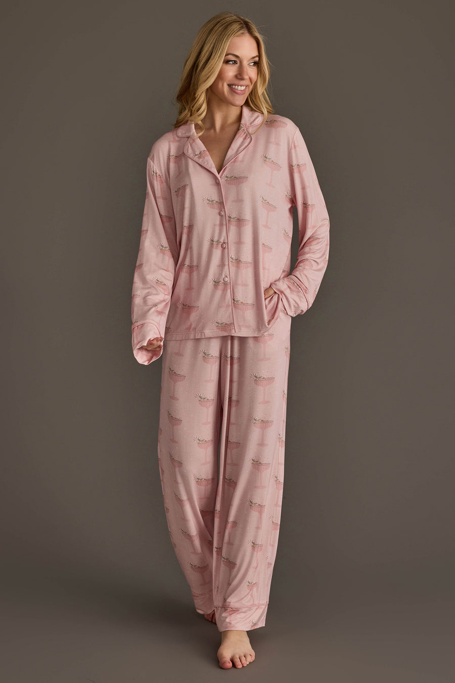 A woman wearing a light pink Christmas Cocktails Jersey Pajama Set featuring a repeating cocktail glass print.