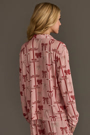 A person wearing a Bows Jersey Pajama Set in light pink with a repeating red and white ribbon bow pattern.