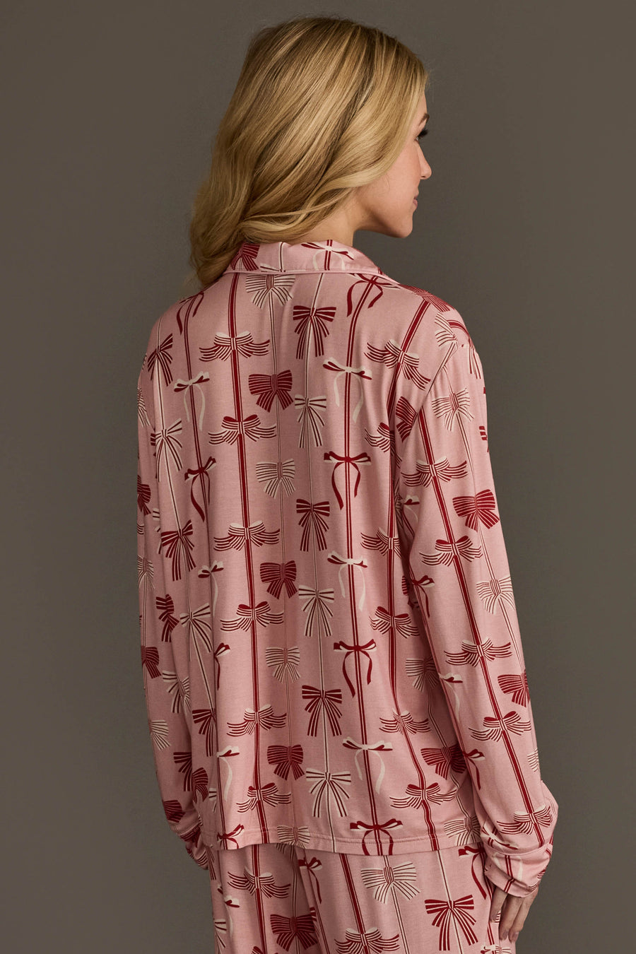 A person wearing a Bows Jersey Pajama Set in light pink with a repeating red and white ribbon bow pattern.