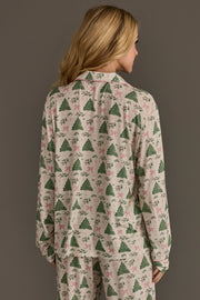 A woman wearing the Trees & Bows Jersey Pajama Set, featuring a festive long-sleeved top and pants with a green Christmas tree and pink bow print.