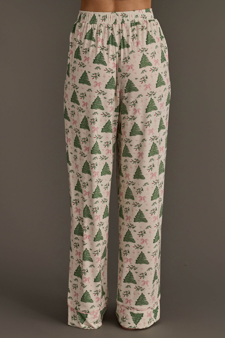 Trees & Bows Jersey Pajama Set featuring light-colored loungewear pants with a repeating pattern of green Christmas trees, pink bows, and holly sprigs.