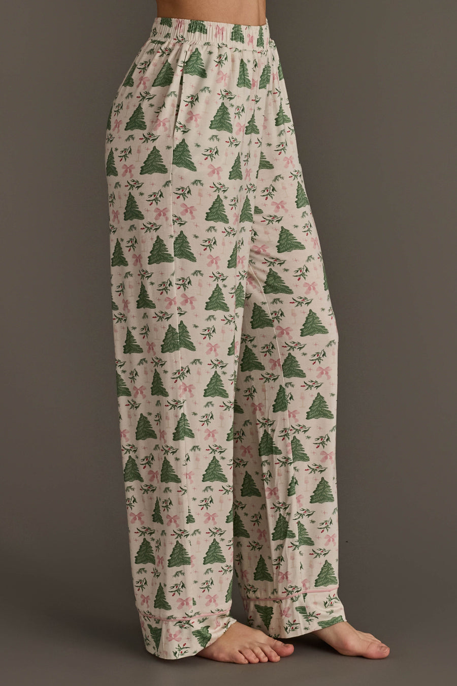 Off-white jersey pajama pants from the Trees & Bows Jersey Pajama Set, featuring a repeating pattern of green Christmas trees and pink bows, an elastic waistband, and pink piped hems.