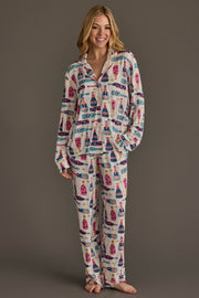 A woman wearing a Champagne Bottles Jersey Pajama Set featuring a festive, repeating pattern of colorful champagne bottles and stars.