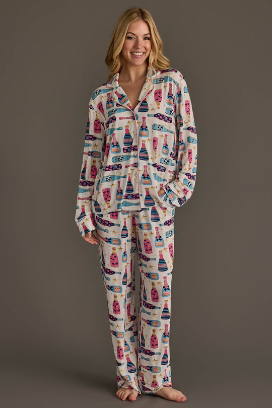 A woman wearing a Champagne Bottles Jersey Pajama Set featuring a festive, repeating pattern of colorful champagne bottles and stars.