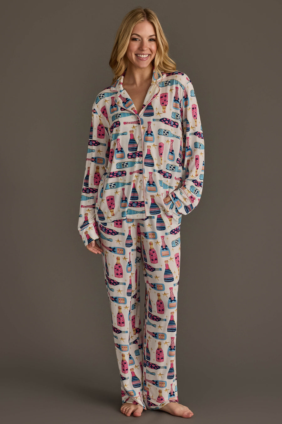 A woman wearing a Champagne Bottles Jersey Pajama Set featuring a festive, repeating pattern of colorful champagne bottles and stars.