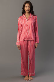 A person wearing a Red & Pink Striped Satin Pajama Set consisting of a long-sleeved button-up shirt and matching pants with red and pink vertical stripes.