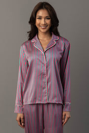 A smiling woman wears a Pink & Green Striped Satin Pajama Set featuring a long-sleeved button-down top and matching pants with pink and green vertical stripes and white piping.