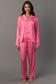 A woman wearing a Bright Pink & Light Pink Striped Satin Pajama Set, featuring a bright and light pink striped button-down top and matching trousers.