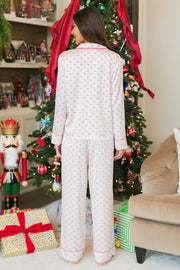 A woman seen from behind, wearing an Ivory & Red Ho Ho Ho Satin Pajama Set with red piping, stands in front of a Christmas tree.