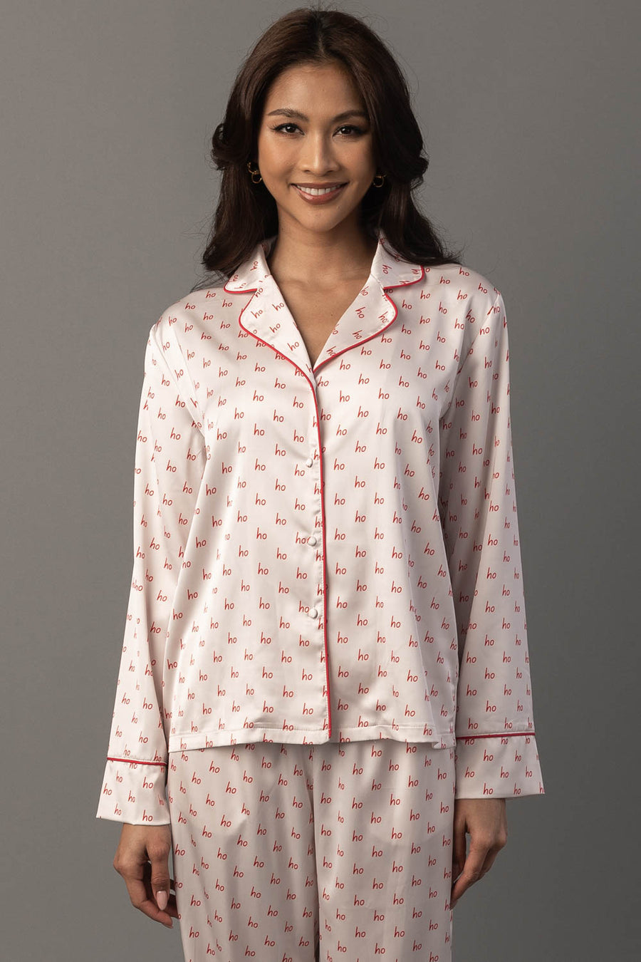 A woman wearing the ivory & red ho ho ho satin pajama set, featuring cream-colored long-sleeve sleepwear with a repeating red ho print and red piping.