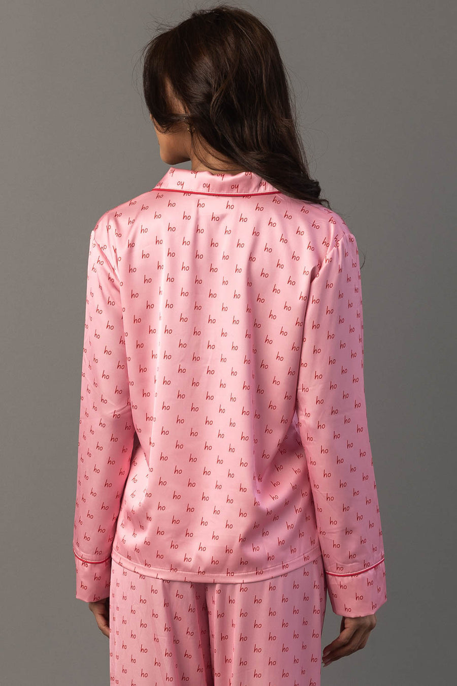 Back view of a person wearing the Light Pink & Red Ho Ho Ho Satin Pajama Set, featuring a light pink satin fabric with a repeating red Ho Ho Ho print and red piping.