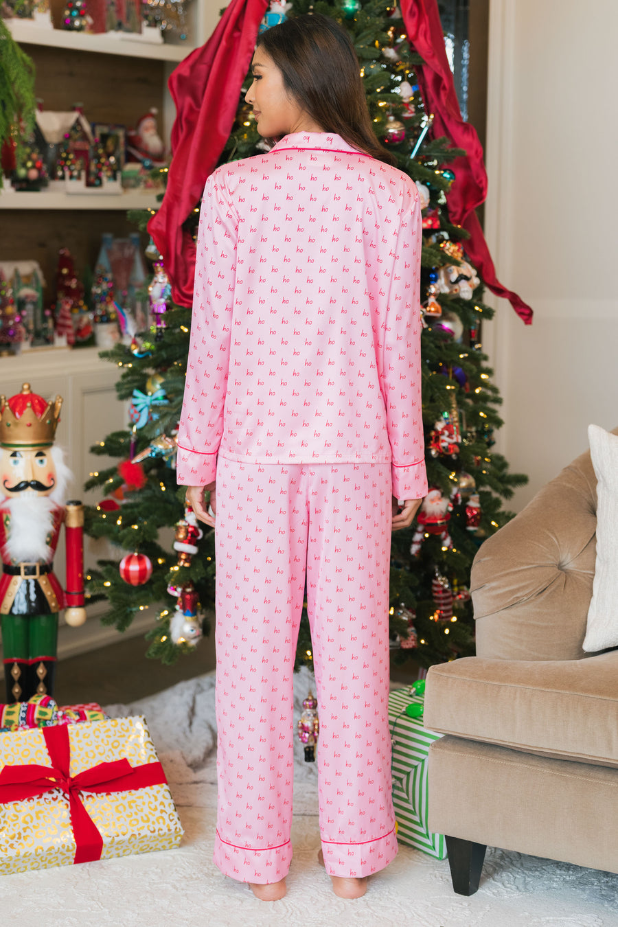 A woman standing in front of a Christmas tree wearing a Light Pink & Red Ho Ho Ho Satin Pajama Set.