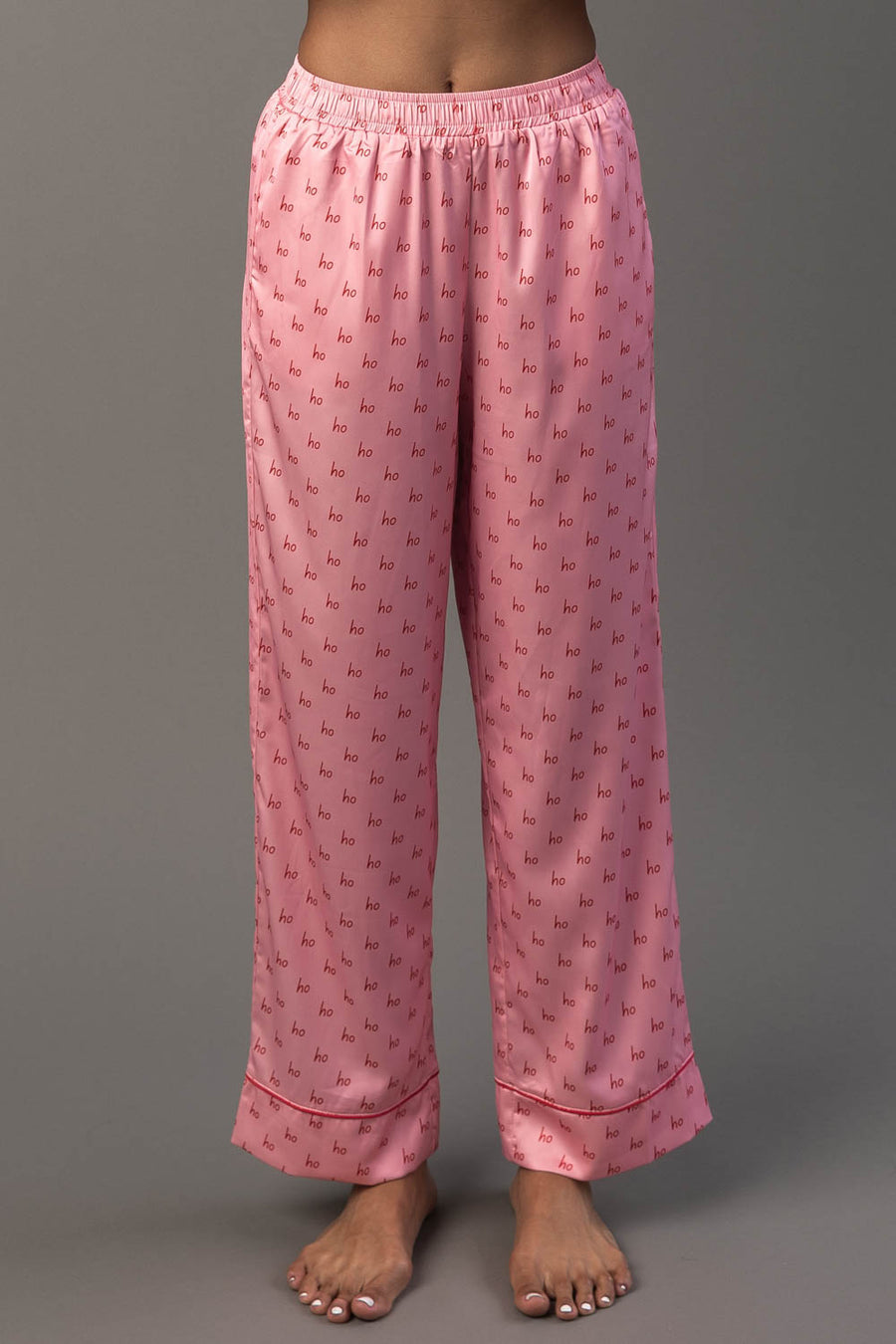 Light Pink & Red Ho Ho Ho Satin Pajama Set pants in light pink featuring a repeating red Ho Ho Ho print and red piping along the hems.