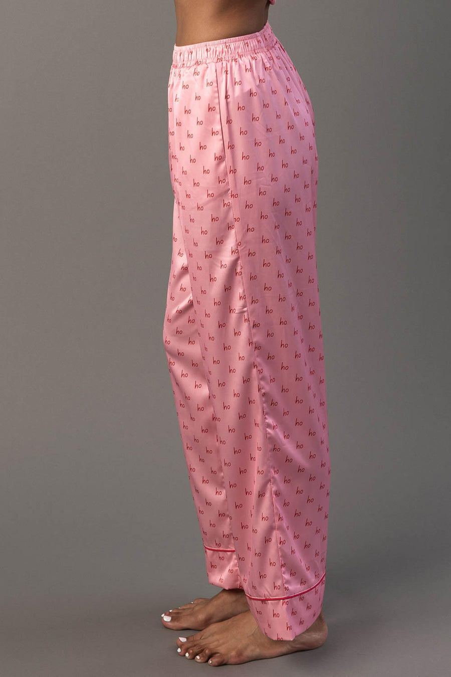 Side view of Light Pink & Red Ho Ho Ho Satin Pajama Set pants in light pink with a repeating red Ho Ho Ho print.