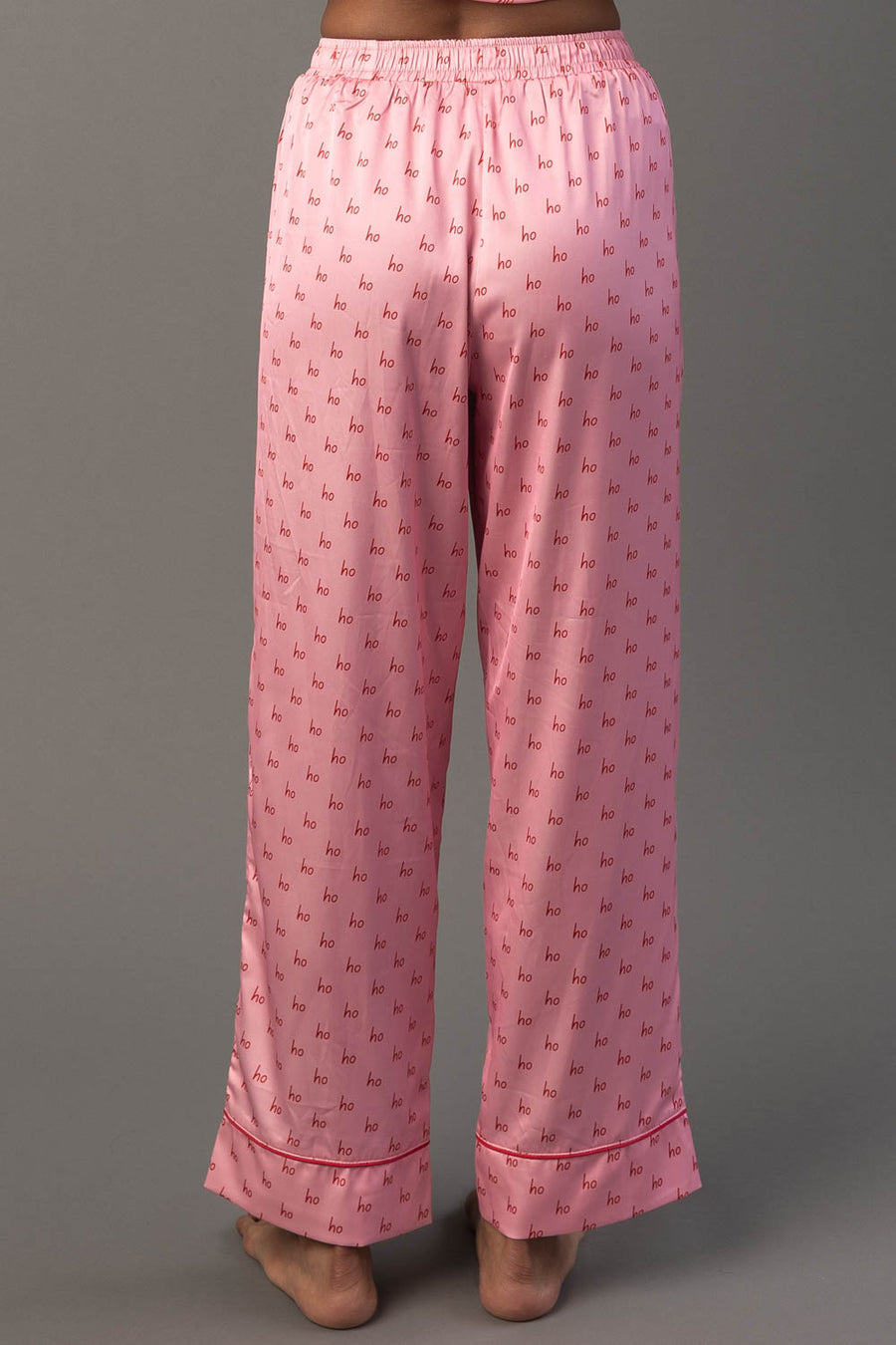 Light Pink & Red Ho Ho Ho Satin Pajama Set pants in light pink featuring a repeating red ho ho ho print and a red hem at the ankles.