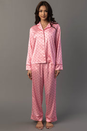 A woman wears a Panache Apparel Collection Light Pink & Red Ho Ho Ho Satin Pajama Set, a light pink satin pajama set featuring a repeating red ho ho ho print and red piping.