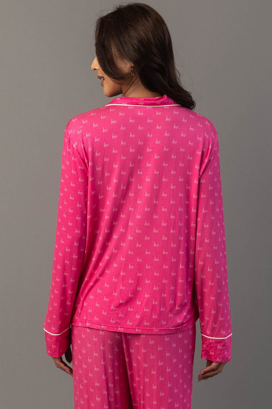 A person wears a Pink & Light Pink Ho Ho Ho Jersey Pajama Set in hot pink with a repeating white ho ho ho print and white piping.
