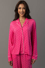 A smiling woman wearing a Pink & Light Pink Ho Ho Ho Jersey Pajama Set featuring a pink button-down top and matching bottoms with a white ho ho ho print.