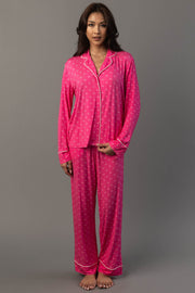 A woman wearing a Pink & Light Pink Ho Ho Ho Jersey Pajama Set featuring bright pink fabric, white piping, and a repeating ho ho ho print.