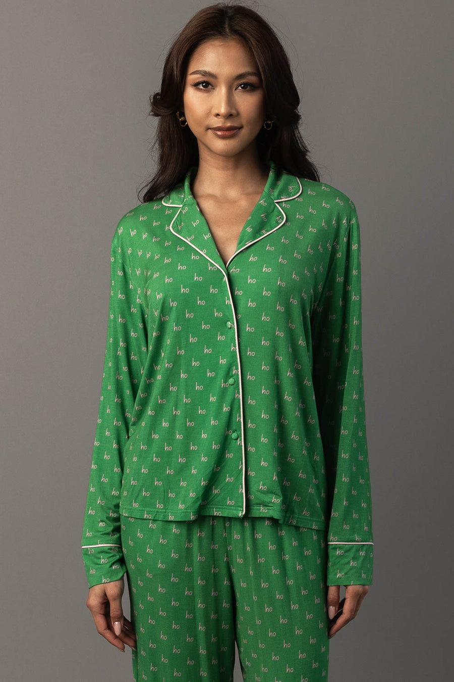 A woman wears a green long-sleeved button-down top from a Green & Light Pink Ho Ho Ho Jersey Pajama Set, patterned with the word ho in light pink.