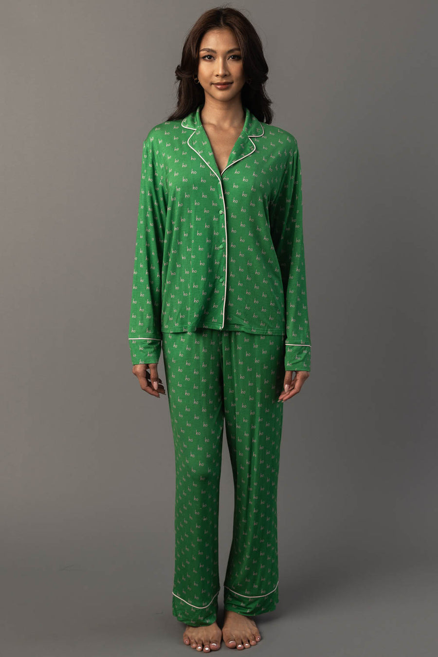 A person wearing a Green & Light Pink Ho Ho Ho Jersey Pajama Set, consisting of a green long-sleeved button-down top with a repeating ho ho ho print and light pink trim.