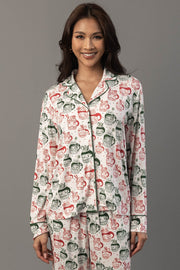 A woman wears an Ivory Santa Mugs Jersey Pajama Set featuring a white long-sleeved button-up shirt and pants covered in a red and green print.