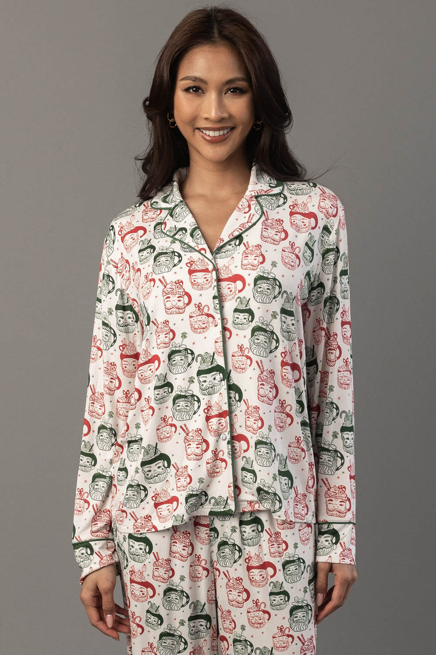 A woman wears an Ivory Santa Mugs Jersey Pajama Set featuring a white long-sleeved button-up shirt and pants covered in a red and green print.