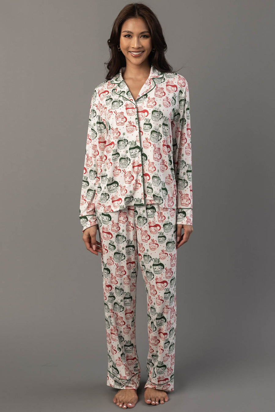 A person wearing an Ivory Santa Mugs Jersey Pajama Set featuring a long-sleeved top and pants patterned with red and green Santa mug illustrations.