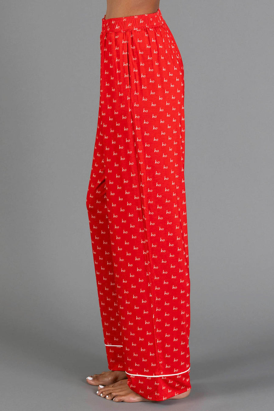Side view of Red & White Ho Ho Ho Jersey Pajama Set pants in red with a repeating white ho ho ho print and white hem piping.