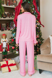 A woman seen from behind wearing a Light Pink & Red Ho Ho Ho Jersey Pajama Set, standing in front of a decorated Christmas tree.