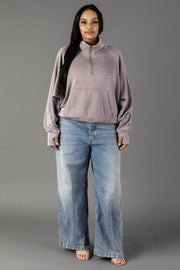 A woman with long dark hair and a relaxed expression stands facing forward against a plain gray background, wearing the Panache Apparel Collection Gray Quarter Zip Sweatshirt, light blue wide-leg jeans, and open-toed heels.