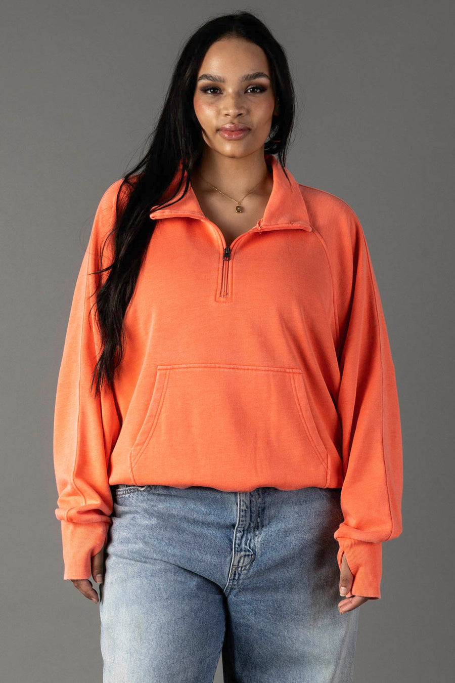 A woman with long dark hair wears the Panache Apparel Collection Coral Quarter Zip Sweatshirt and light blue jeans, standing against a plain gray background with a neutral expression.