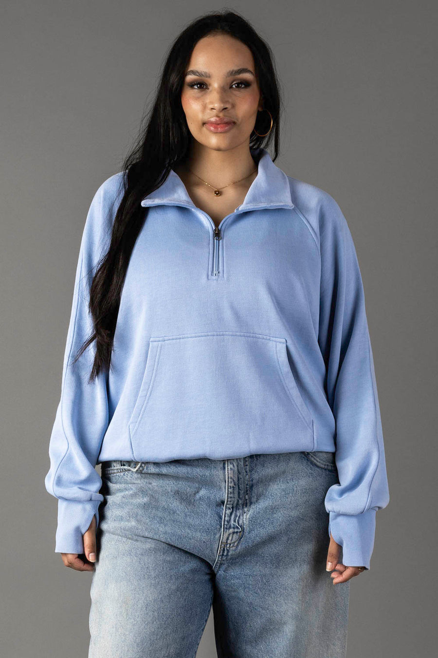 A woman with long dark hair models the Panache Apparel Collection Light Blue Quarter Zip Sweatshirt and light-wash jeans, standing against a plain gray background.